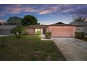 Charming single-story home featuring an attached garage, well-maintained lawn, and lovely landscaping at dusk at 10820 Hachita Dr, Port Richey, FL 34668