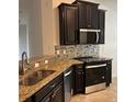 Well-equipped kitchen featuring dark wood cabinets, granite countertops, stainless steel appliances, and decorative backsplash at 12055 Cardinal Flower Dr, Riverview, FL 33579