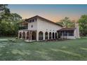 Expansive stucco home with arched loggia, covered balcony, and a lush lawn against wooded backdrop at 12311 Oakwood Dr, Hudson, FL 34669