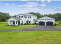 Stunning two-story white home with metal roof, manicured lawn, and three car garage at 13711 Lussier Ln, Spring Hill, FL 34610