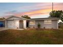 Charming single-story home with a well-maintained lawn, attached garage, and freshly painted exterior, glowing at sunset at 2252 Society Dr, Holiday, FL 34691