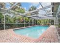 Enclosed in-ground pool surrounded by brickwork and lush greenery, ideal for relaxation and outdoor enjoyment at 3230 Player Dr, New Port Richey, FL 34655