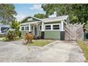 Green home featuring a black door, front yard plants, quaint front porch, and wood fence at 6006 N Highland Ave, Tampa, FL 33604
