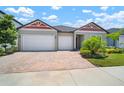 Beautiful single-story home featuring a three-car garage, brick driveway, and landscaped garden at 21648 Snowy Orchid Ter, Land O Lakes, FL 34637