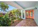 Inviting front porch with brick flooring, colorful plants, and a bright orange front door at 3749 Mckay Creek Dr, Largo, FL 33770
