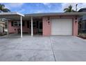 Charming pink single-story home featuring a covered carport and white garage door, complemented by tropical palm tree accents at 5445 Manatee Point Dr, New Port Richey, FL 34652