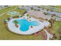 Aerial view of a luxurious community pool, featuring a spacious deck, palm trees, and covered seating areas at 11524 Sage Canyon Dr, Riverview, FL 33578