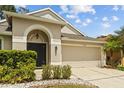 Elegant entrance with dark door, manicured shrubbery, and a wide driveway leading to a two-car garage at 25332 Lexington Oaks Blvd, Wesley Chapel, FL 33544
