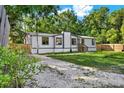 Exterior view of home with a gravel driveway, green lawn, and partially wooded area offering privacy at 9690 Jerome Dr, New Port Richey, FL 34654