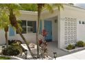Close up of a white home's front entrance, featuring a blue door, palm trees and lush tropical foliage at 9639 Mainlands E Blvd, Pinellas Park, FL 33782