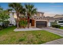 Two-story home with green lawn, landscaping, palm trees, a two-car garage, and neutral colored exterior at 7705 S Sparkman St, Tampa, FL 33616