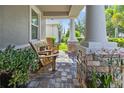 Relaxing front porch featuring stone pillars, brick flooring, comfortable wooden chairs, and lush potted plants at 12009 Whistling Wind Dr, Riverview, FL 33569