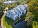 Aerial view of a multi-story condo building with a metal roof, surrounded by trees and a pond with wooden walkway at 2533 Dolly Bay Dr # 203, Palm Harbor, FL 34684