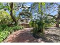 A picturesque view of a brick driveway leading to a tan home surrounded by mature trees and tropical foliage at 8350 40Th N Ave, St Petersburg, FL 33709