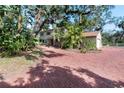 Wide view of a home's tan exterior with brick driveway and tropical landscaping beneath a canopy of shady trees at 8350 40Th N Ave, St Petersburg, FL 33709