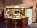 Open kitchen with wood cabinets, skylight, white refrigerator, and breakfast bar with seating at 11430 Nature Trl, Port Richey, FL 34668