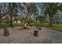 Outdoor fire pit area with gravel base and log seating surrounded by mature trees and lush green grass at 11441 Hammock Oaks Ct, Lithia, FL 33547