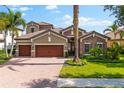Charming home with a brick driveway, three-car garage, lush landscaping, and elegant stone and stucco facade at 1416 Via Verdi Dr, Palm Harbor, FL 34683