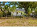 Quaint cottage-style home with a black fence, lush landscaping, and mature trees at 1216 E Lambright St, Tampa, FL 33604