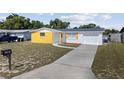 View of a single-story home showcasing its yellow accent wall, long driveway, and well-maintained lawn at 12901 College Hill Dr, Hudson, FL 34667