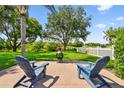 Relaxing backyard with Adirondack chairs, a fire pit, and a lush lawn surrounded by trees and a white fence at 13028 Prestwick Dr, Riverview, FL 33579