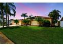 Charming single-story home featuring a well-manicured lawn and lush tropical landscaping at dusk at 13028 Prestwick Dr, Riverview, FL 33579