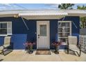 Welcoming front entrance to a blue home with a white door, awning, and potted plants, creating a cozy curb appeal at 13920 Berkowitz Ave, Hudson, FL 34667