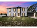 Two-story home at dusk with a two-car garage, dark trim, light siding, and arched entryway at 12470 Elgin Blvd, Spring Hill, FL 34609