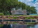 Attractive neighborhood entrance with stone features, landscaping, and a serene pond reflecting the sky at 3909 Valrico Grove Dr, Valrico, FL 33594