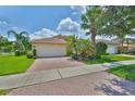 Charming single-story home with a two car garage, brick driveway, and tropical landscaping at 16227 Cape Coral Dr, Wimauma, FL 33598