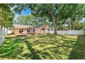 Spacious backyard with lush green grass, mature trees for shade, a white fence, and a wooden deck with outdoor seating at 11510 92Nd Way, Largo, FL 33773