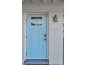 Close-up of a charming light blue front door with decorative window, house number, and exterior light fixture at 10664 Starkey Rd, Seminole, FL 33777