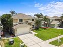 Charming tan two-story home with an attached garage, lush green lawn, and tropical trees at 4852 Trinidad Dr, Land O Lakes, FL 34639