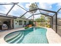 Backyard view of a screened pool featuring a tile pool deck, tropical plants and a hot tub in a partially fenced yard at 2048 Douglas Ave, Dunedin, FL 34698