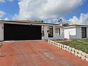 Single-story white house with a black garage door and red driveway on a partially sunny day at 7834 Treasure Pointe Dr, Port Richey, FL 34668