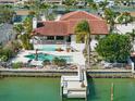 Aerial view of a waterfront home with a pool, dock, well maintained landscaping, and tile roof at 11285 8Th E St, Treasure Island, FL 33706