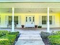 Inviting front porch with tiled floor, white columns and front door, with views of the landscaped yard at 1914 Henley Rd, Lutz, FL 33558