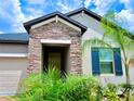 A welcoming front entrance with stone accents, a covered porch, and tropical landscaping at 24815 Lambrusco Loop, Lutz, FL 33559