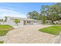 Wide brick driveway leading to a white brick home, complemented by lush green lawn and mature trees at 2554 Lake Ellen Cir, Tampa, FL 33618