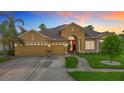 Inviting single-story home features a three-car garage, red front door, and manicured landscaping at dusk at 1443 Obear Ct, Wesley Chapel, FL 33543