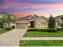 Charming one-story home with a well-manicured lawn, a two-car garage, and inviting curb appeal at sunset at 17610 Buckingham Garden Dr, Lithia, FL 33547
