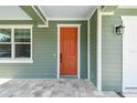 Close up of the vibrant orange front door, complemented by stone tile and green siding at 511 Roanoke St, Dunedin, FL 34698