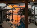 Beautiful screened pool featuring a sunset view, palm trees, rock waterfall features, and serene waterfront views at 5225 Brighton Shore Dr, Apollo Beach, FL 33572