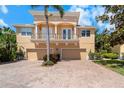 Charming two-story home featuring a balcony, three-car garage, brick driveway, and lush landscaping at 191 Banyan Bay Dr, St Petersburg, FL 33705