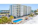 Exterior view of a beachfront condo with a pool, lounge chairs, and tiki umbrellas at 13500 Gulf Blvd # 506, Madeira Beach, FL 33708