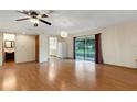 Open living room with hardwood floors, ceiling fan, sliding glass doors, and an open doorway at 5250 Brody Blvd, Wimauma, FL 33598