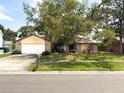 A charming single-story home features a mature tree, a two-car garage, and a well-maintained lawn at 1228 Rainbrook Cir, Valrico, FL 33596