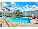 A screened-in pool area featuring an in-ground pool, brick pavers, outdoor seating, and lush landscaping at 6219 Wendell Dr, Wesley Chapel, FL 33544
