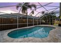 Screened-in pool featuring a unique shape surrounded by light-colored stone pavers with a view of the fenced yard at 10516 Gretna Green Dr, Tampa, FL 33626