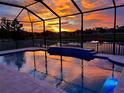 Relaxing screened-in pool with a tiled patio reflecting a vibrant sunset over the neighboring pond at 18827 Henequen Lane, Spring Hill, FL 34610